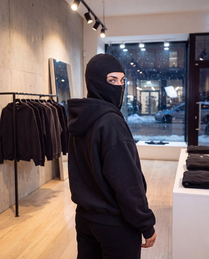 Woman in a clothing store looking over her shoulder, the Cover Hoodie zipped up and the outer hood down